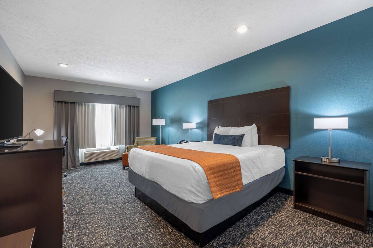 Habitación de hotel con una cama grande, dos lámparas de noche, un escritorio con lámpara, una silla y una ventana con cortinas.