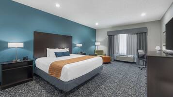 Een hotelkamer met een groot bed, twee nachtkastjes met lampen, een bureau, een stoel, een raam met gordijnen en een radiator.