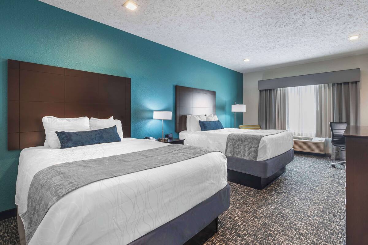Habitación de hotel con dos camas, un escritorio y un ventanal con cortinas.
