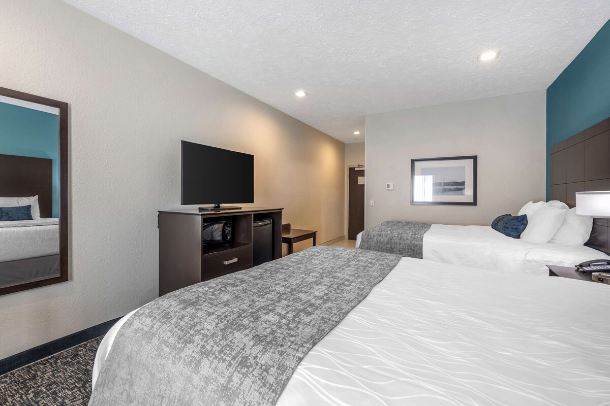 A hotel room with two beds, a desk, a television, and a framed picture on the wall.