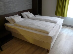 Un lit double avec du linge de lit blanc, une tête de lit en bois et une étagère intégrée.