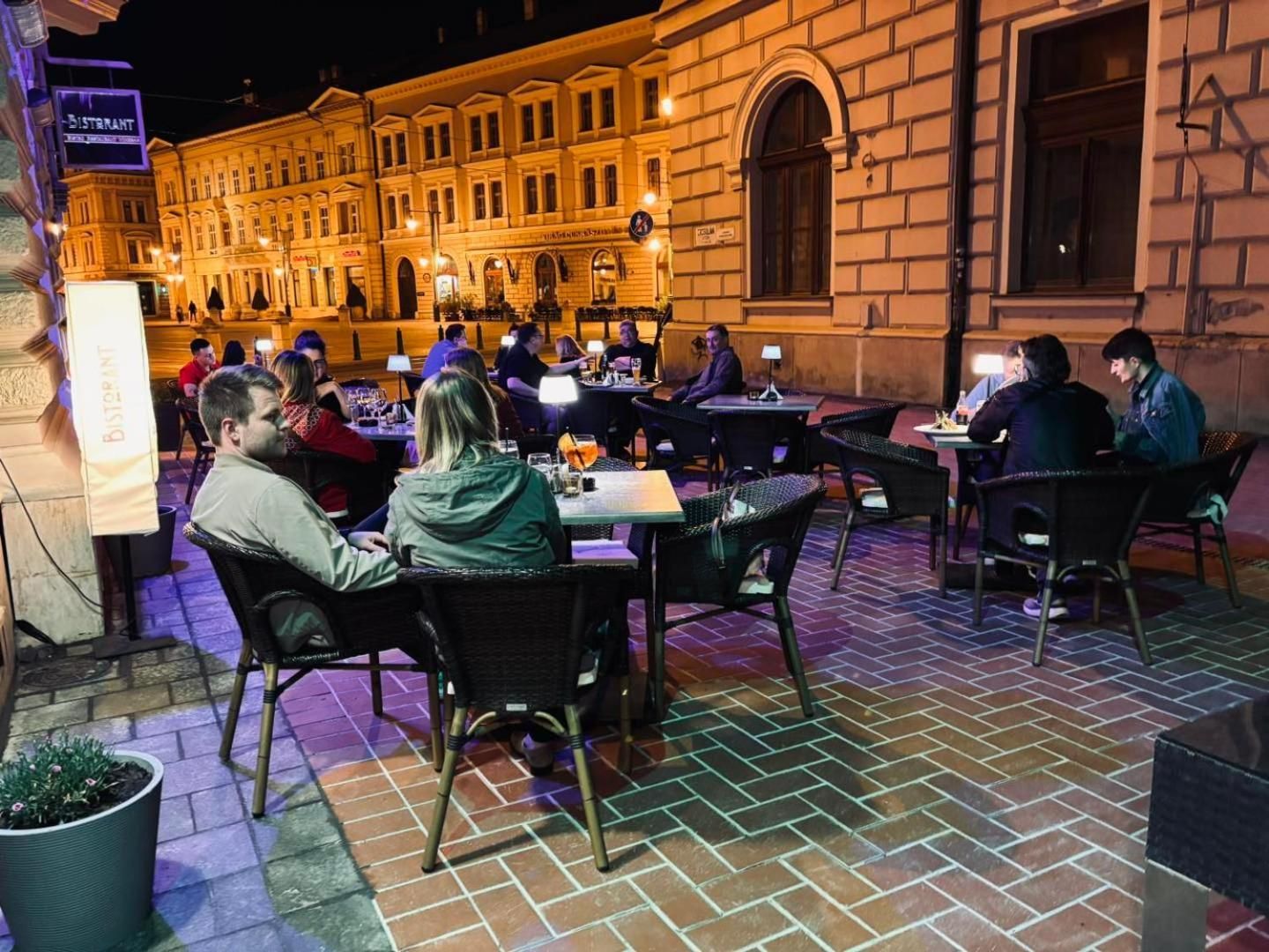 An outdoor dining area with brick flooring and tables, surrounded by a building with classical architecture.