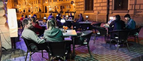 Un espacio exterior para comer con suelo de ladrillo y mesas, rodeado por un edificio de arquitectura clásica.