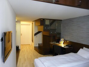 A hotel room with a bed, a desk, a chair, a TV, and a wardrobe.