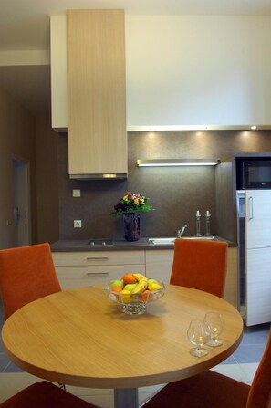 Une cuisine moderne avec une table à manger, des chaises, un panier de fruits et un verre à vin.