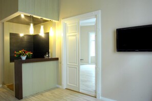 Un espace d’accueil avec un comptoir de réception en bois foncé, un téléviseur à écran plat fixé au mur et une porte donnant sur une autre pièce.