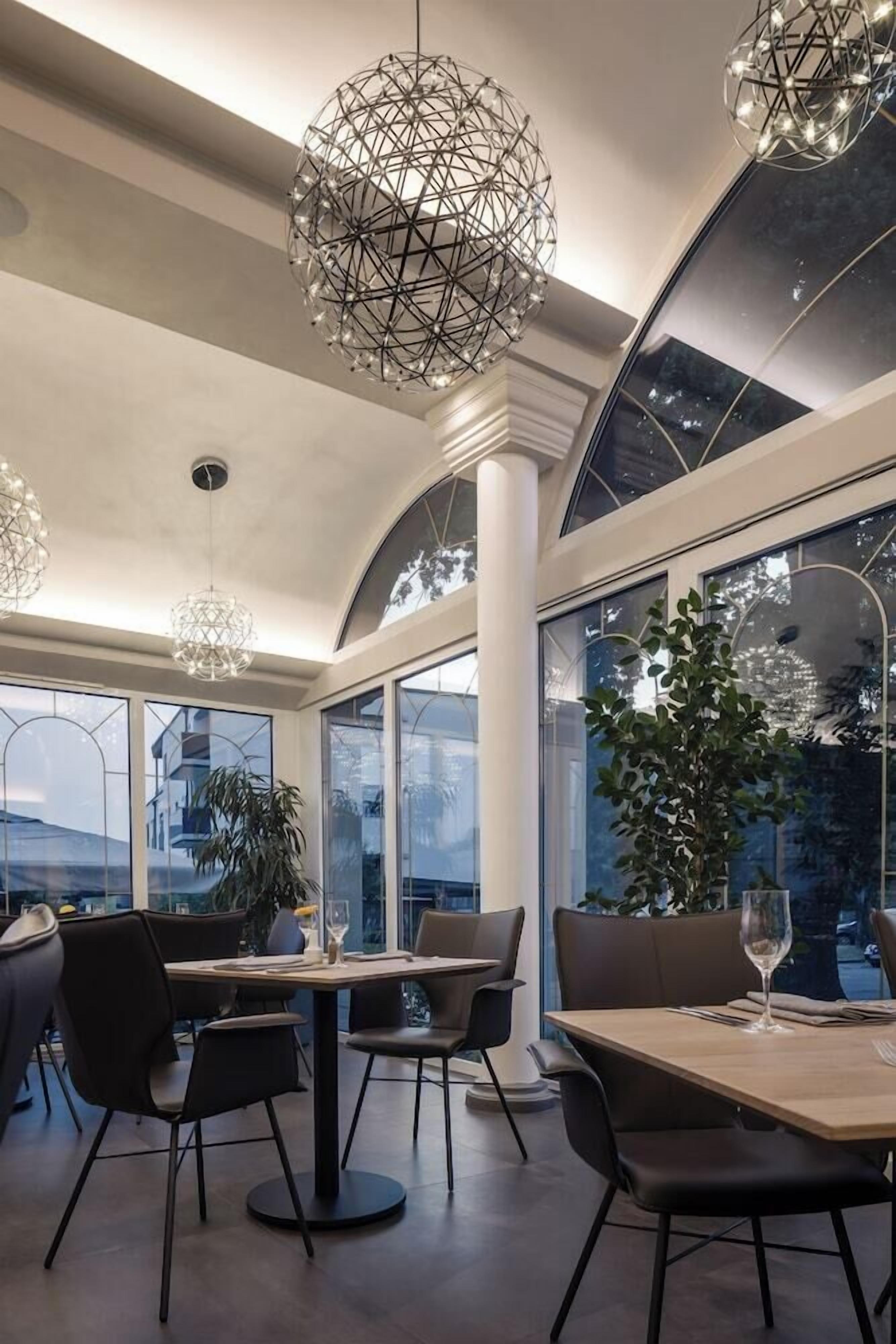 A modern dining area with geometric chandeliers, large windows, and a view of the outdoors.