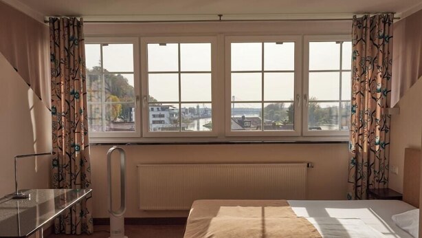 Una habitación de hotel con cama, escritorio, radiador y ventana con cortinas.