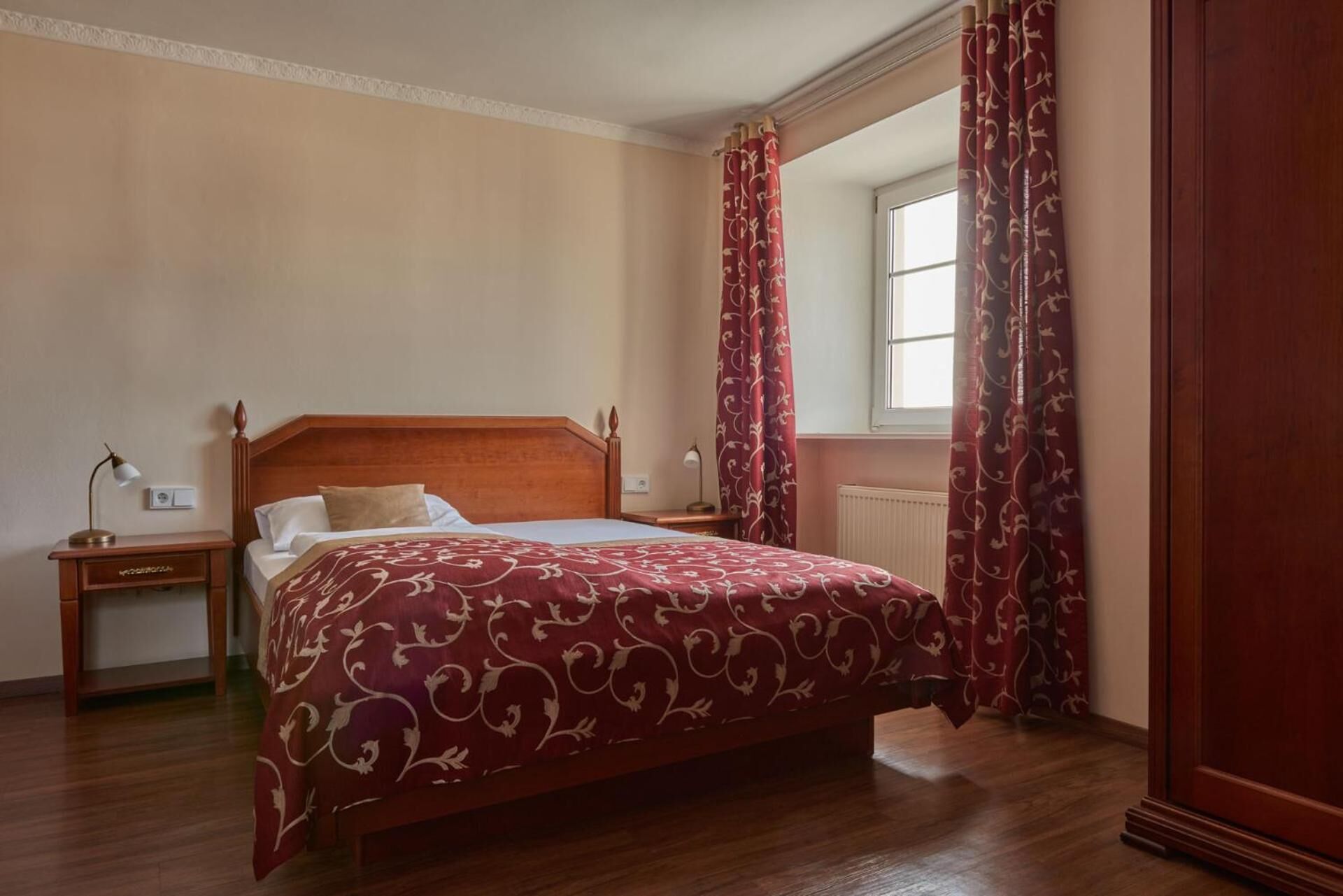 Een slaapkamer met een houten bed, een nachtkastje, een lamp en een raam met gordijnen.