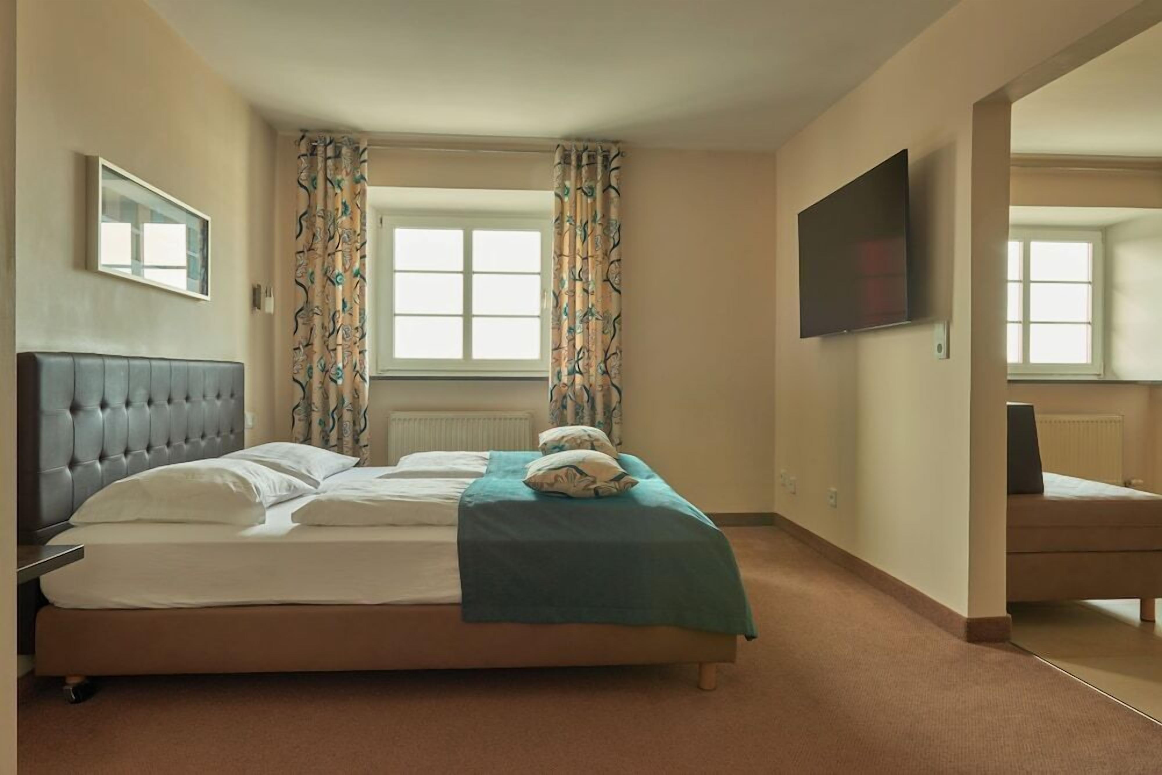 A hotel room with a large bed, a television, a window with curtains, and a framed picture on the wall.