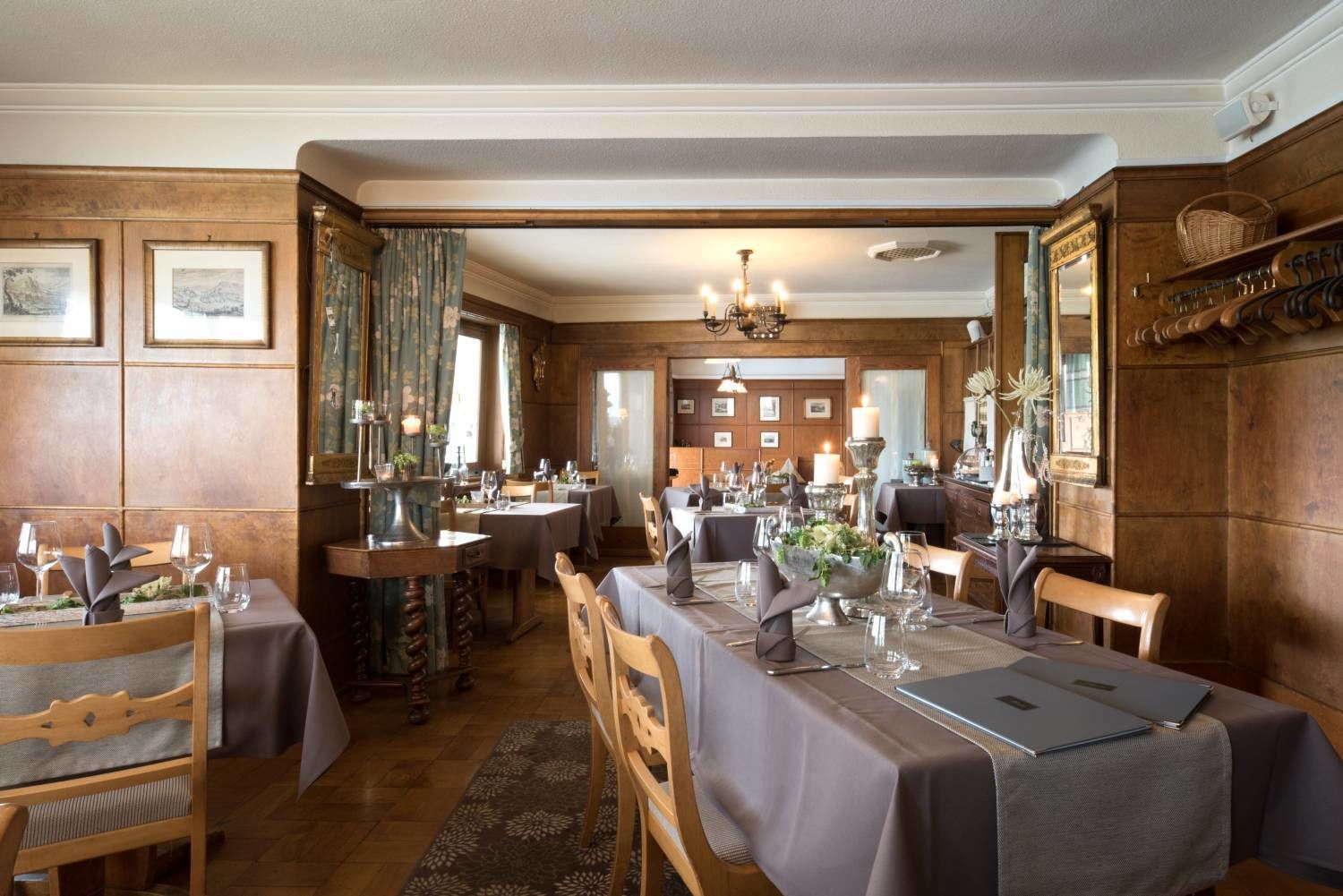 A restaurant with multiple tables set for dining, wooden paneling on the walls, and a chandelier.