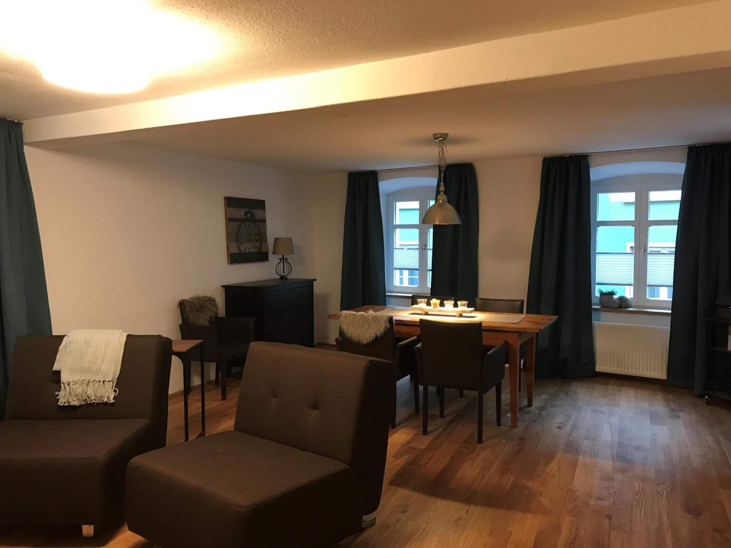 Een gezellige woonkamer met een bank, een eettafel met stoelen, een lamp en een open haard.