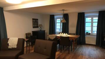 Een gezellige woonkamer met een bank, een eettafel met stoelen, een lamp en een open haard.