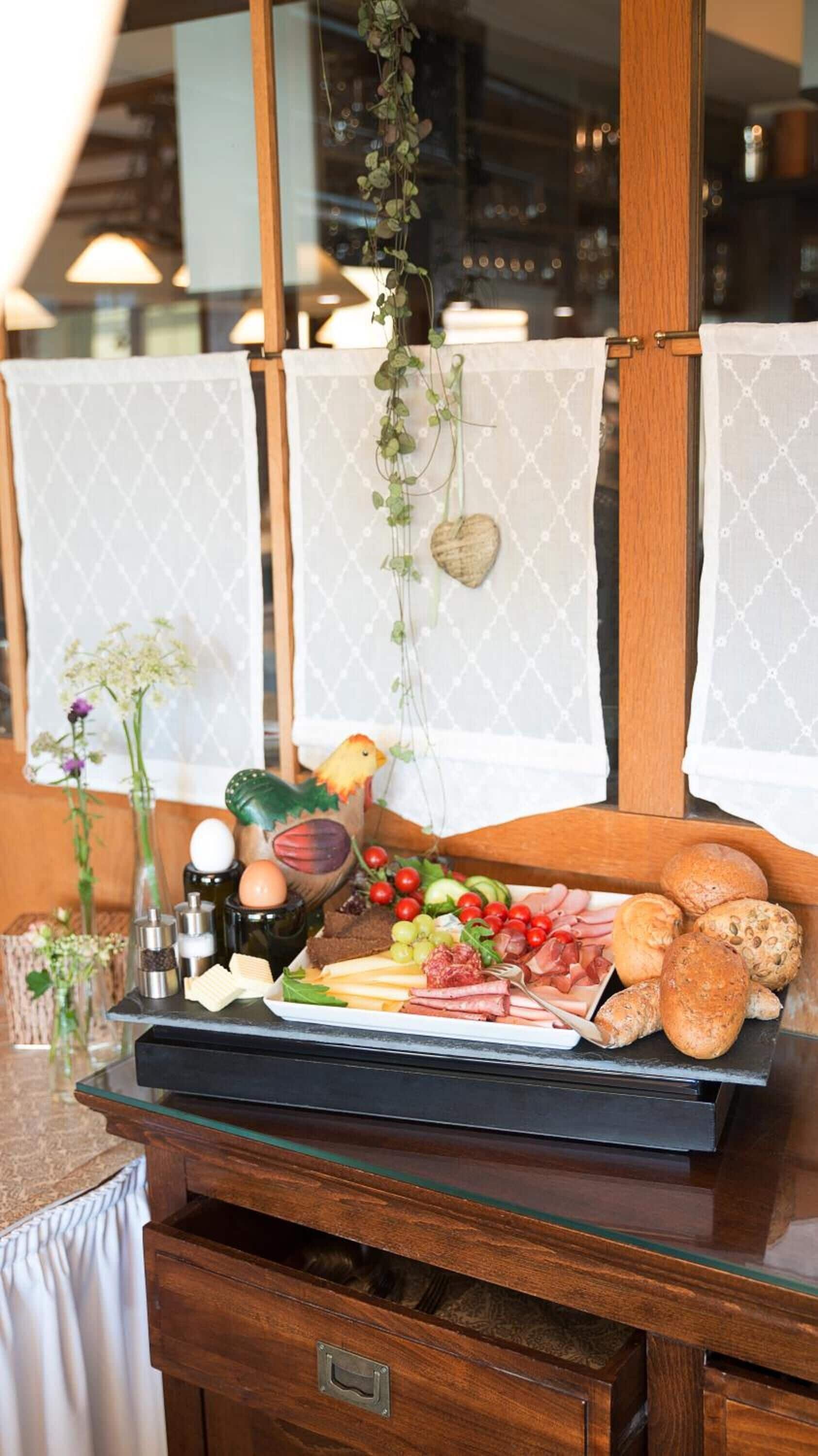 Ein Holztisch mit einer Wurstplatte, einer Blumenvase und einer hängenden Pflanze.