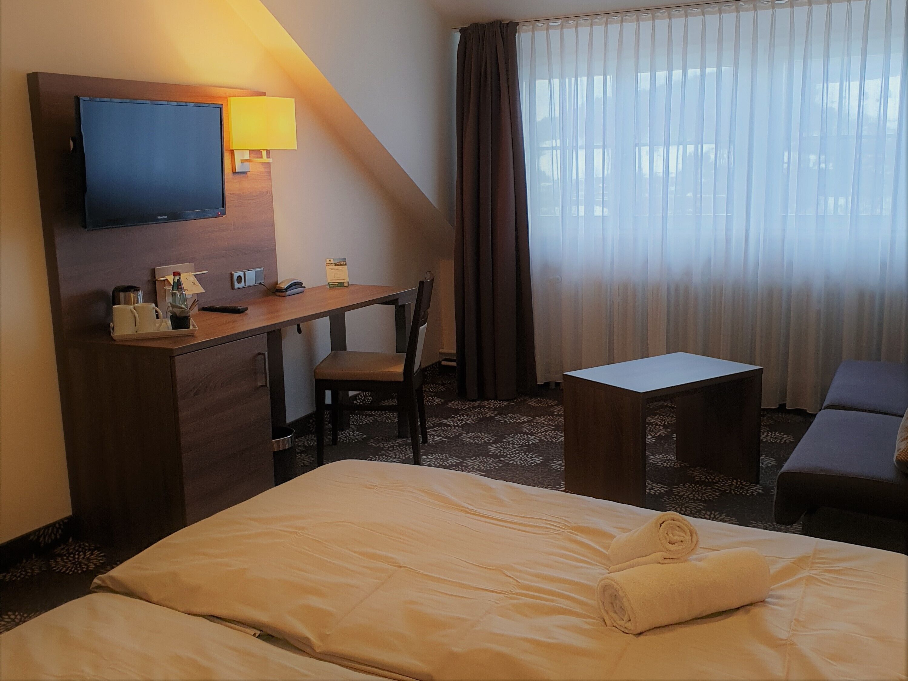A hotel room with a bed, a desk, a chair, a television, and a window with curtains.