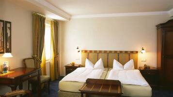 A hotel room with two beds, a desk, a chair, a small table, and a lamp.