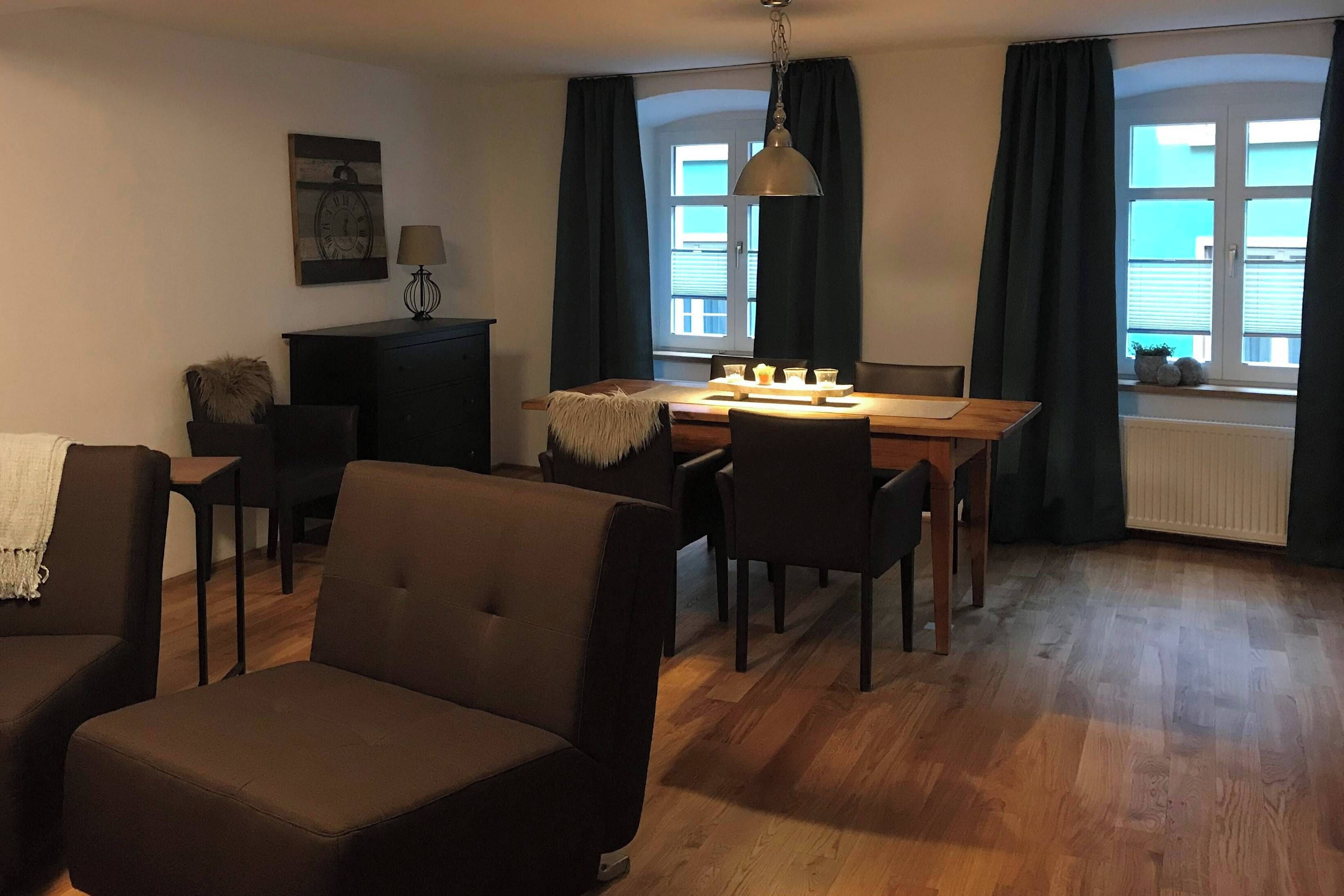 Una sala de estar con un sofá, una mesa de comedor con sillas, una lámpara y una ventana con cortinas.