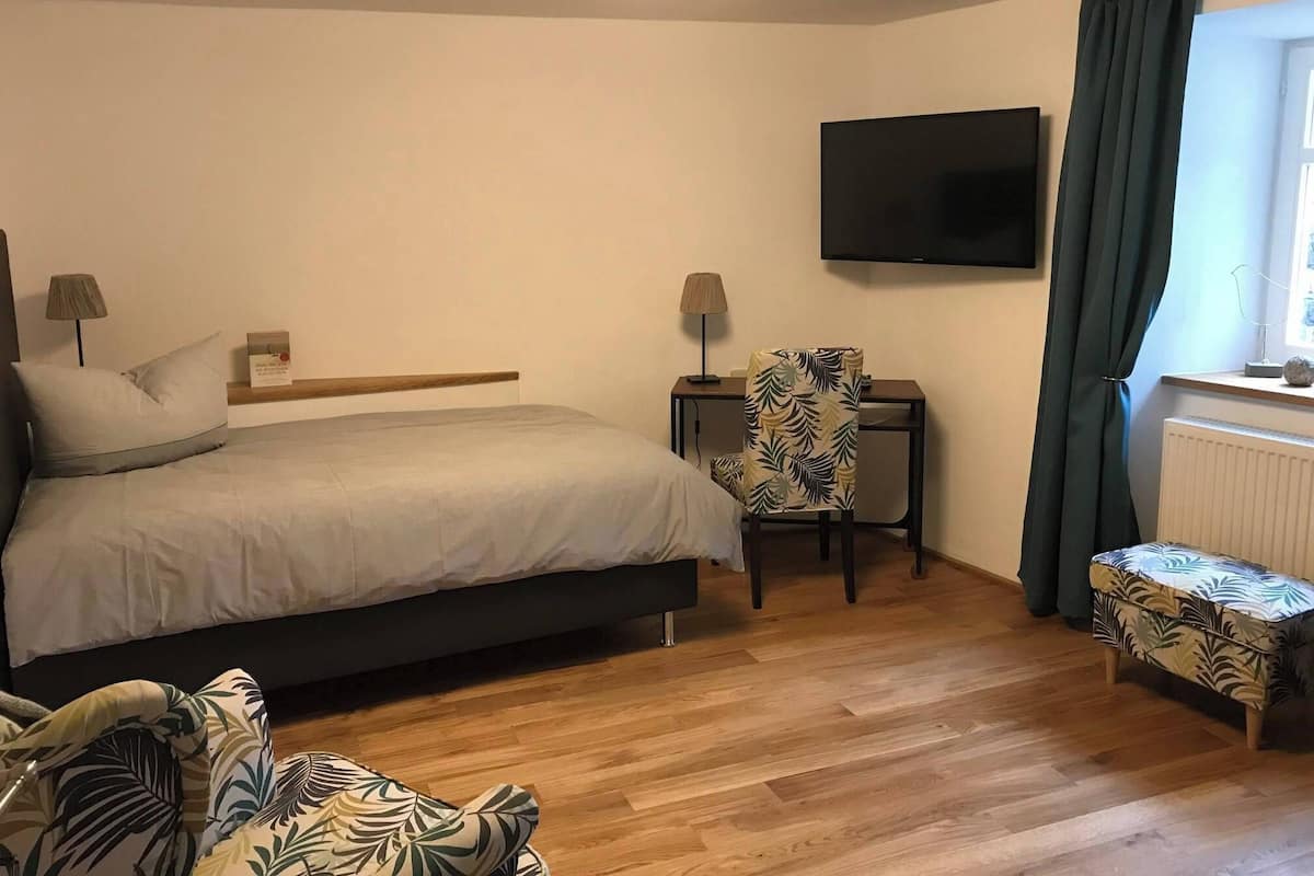 Hotellihuone, jossa on sänky, työpöytä, tuoli, televisio ja ikkuna, jossa on verhot.