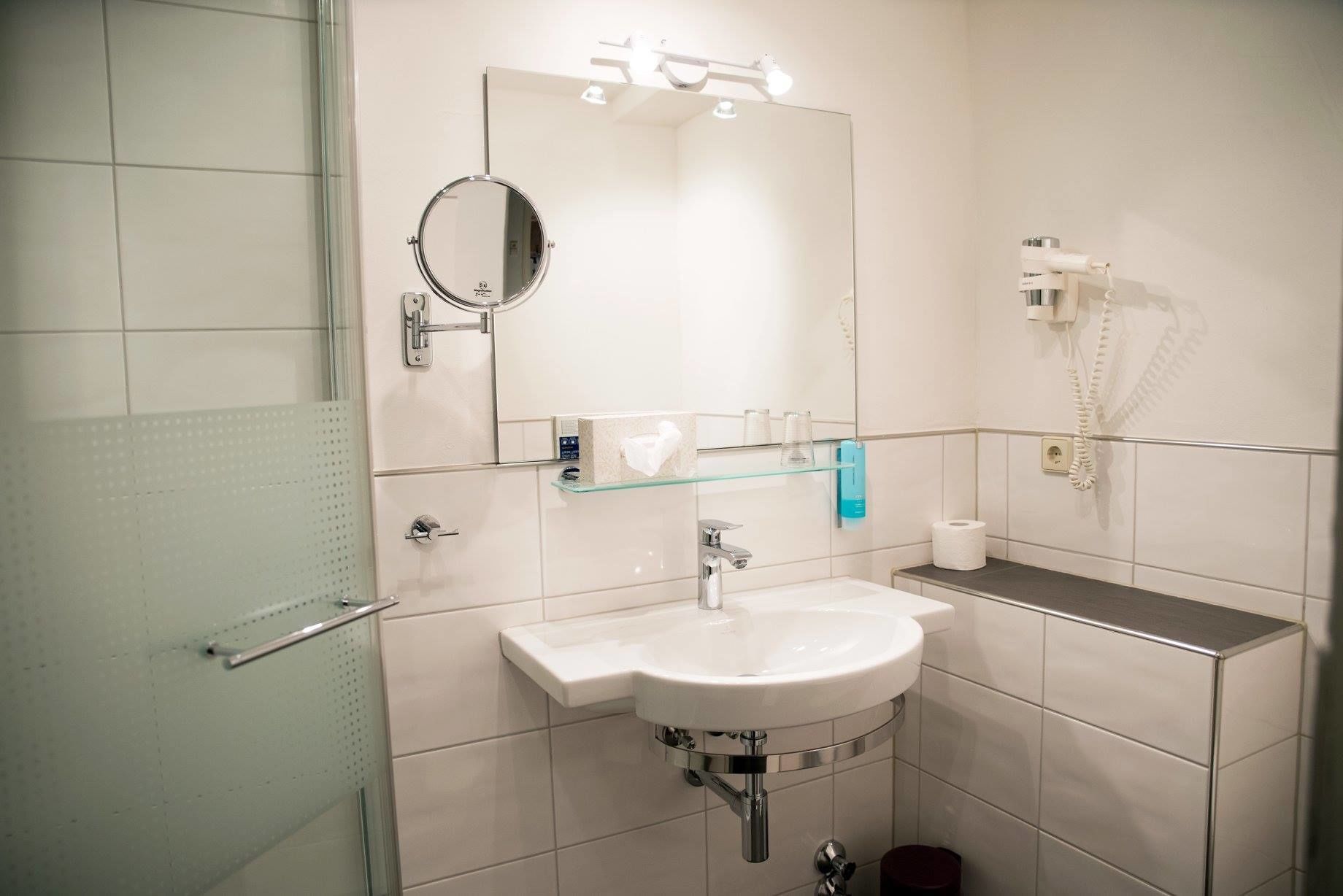 A modern bathroom with a white sink, mirror, and glass shelf.