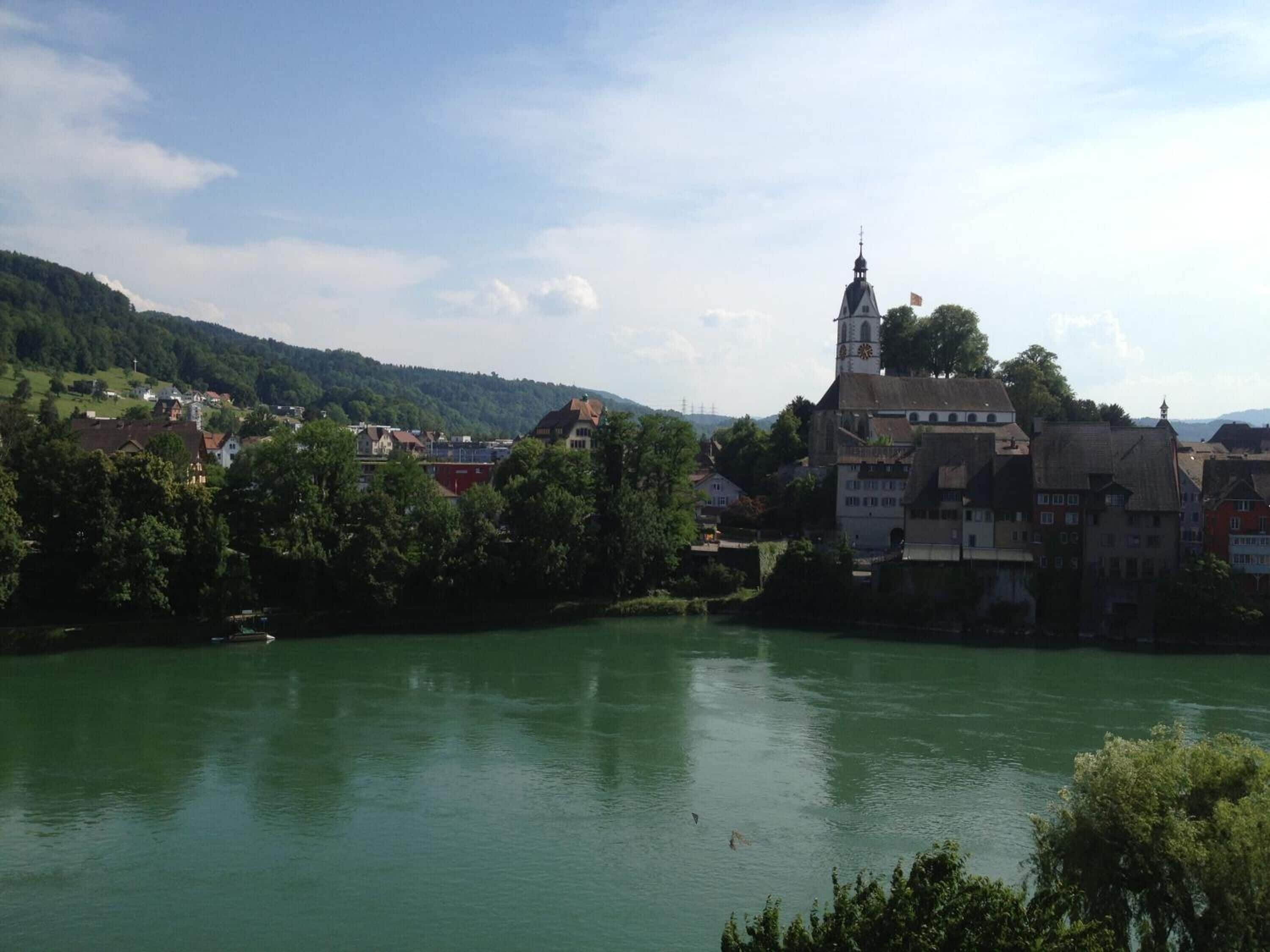 A riverside town with historic buildings, a prominent church tower, and a calm river.