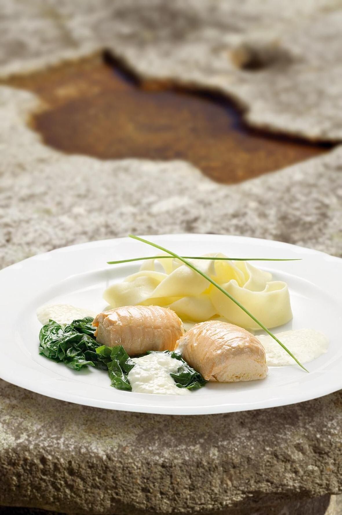 A plate of food with a creamy sauce, a green leafy vegetable, and a white sauce on a white plate.