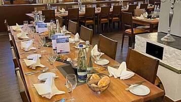 A restaurant with multiple dining tables set for service, wooden flooring, and large windows with curtains.