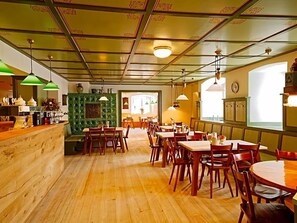 A restaurant interior with wooden flooring, green and white tiled walls, and multiple dining tables and chairs.