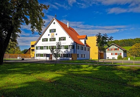 Un bâtiment à deux étages, avec un toit rouge, une façade blanche et des volets verts.