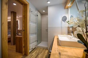 A bathroom with a wooden vanity, a sink, a mirror, and a shower area.