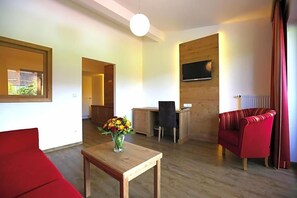 A living room with a red sofa, a wooden coffee table with a vase of flowers, a TV mounted on the wall, and a red armchair.