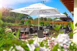 An outdoor seating area with tables and chairs, umbrellas, and a view of a building in the background.