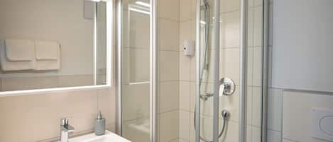 A modern bathroom with a glass-enclosed shower, a white sink with a mirror above it, and a toilet to the right.
