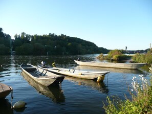 Three boats docked at a calm river with a forested hill in the background. - Hotel Mainblick (Marktheidenfeld)