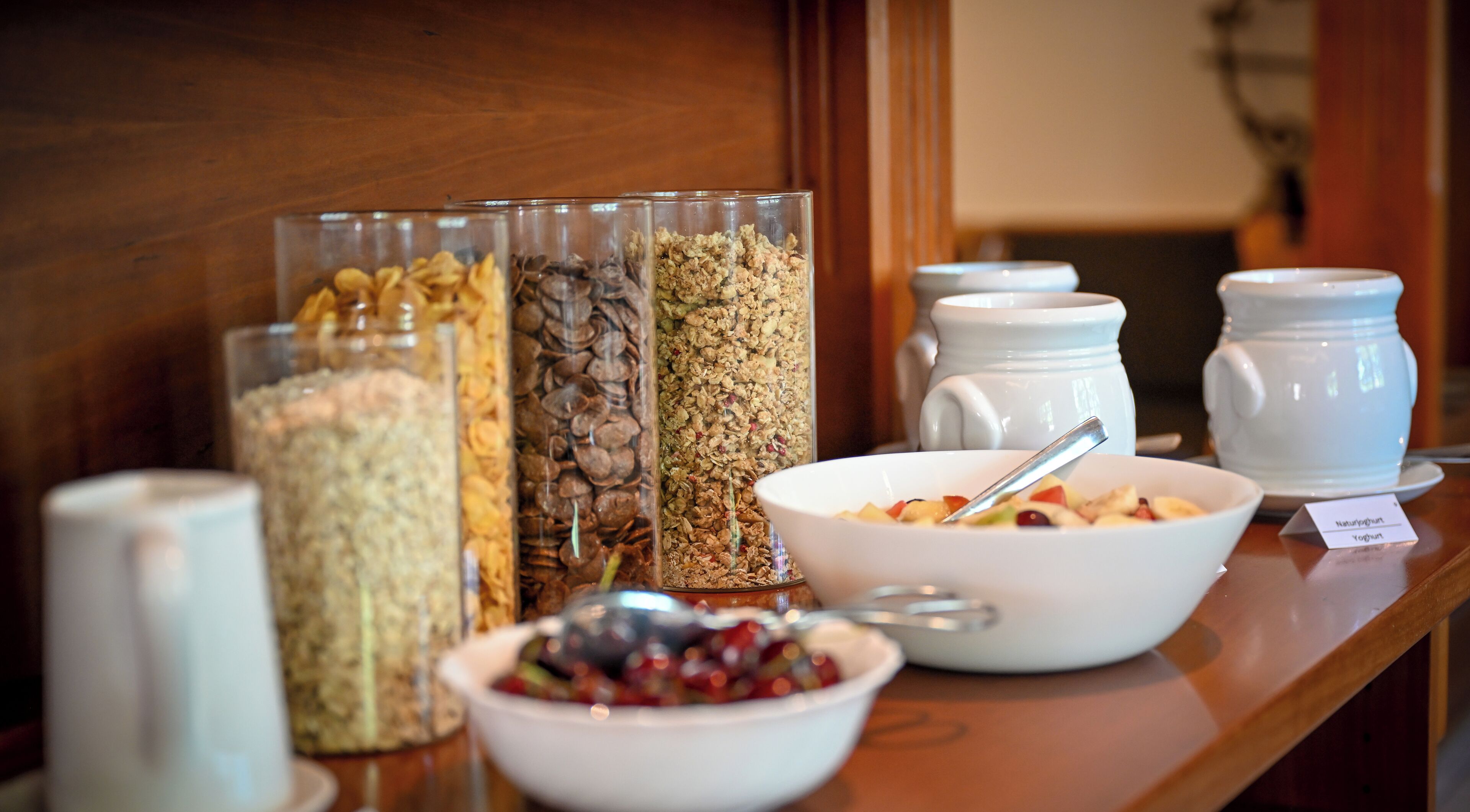 A breakfast buffet with various food options including cereals, fruits, and yogurt.