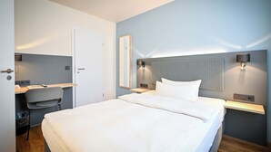 A modern hotel room with a bed, a desk, and a chair.