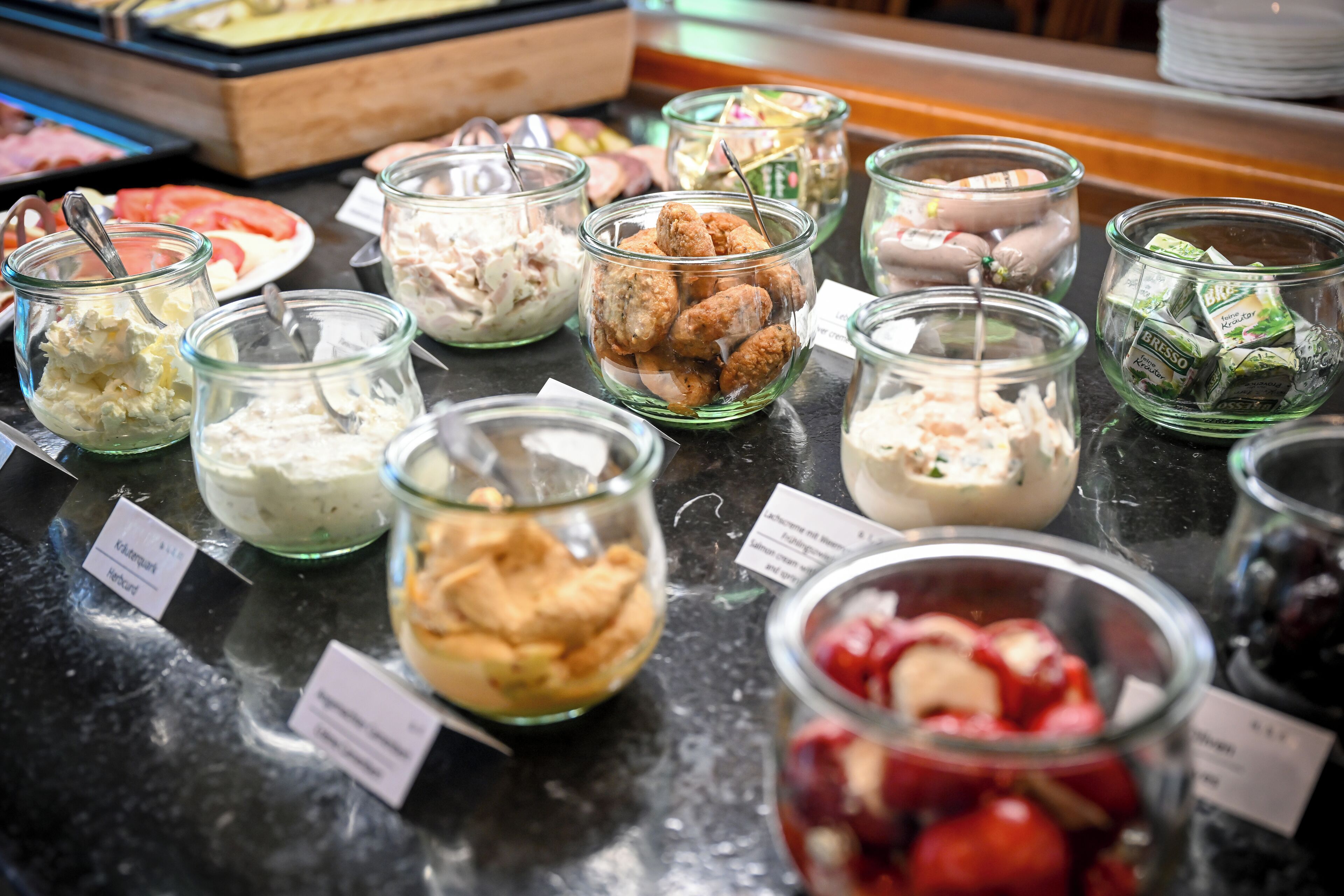 A buffet with various food items in glass containers, including salads, meats, and desserts.