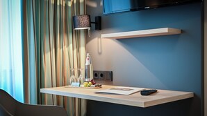 A hotel room with a wooden desk, a bottle of water, a glass of wine, and a remote control.