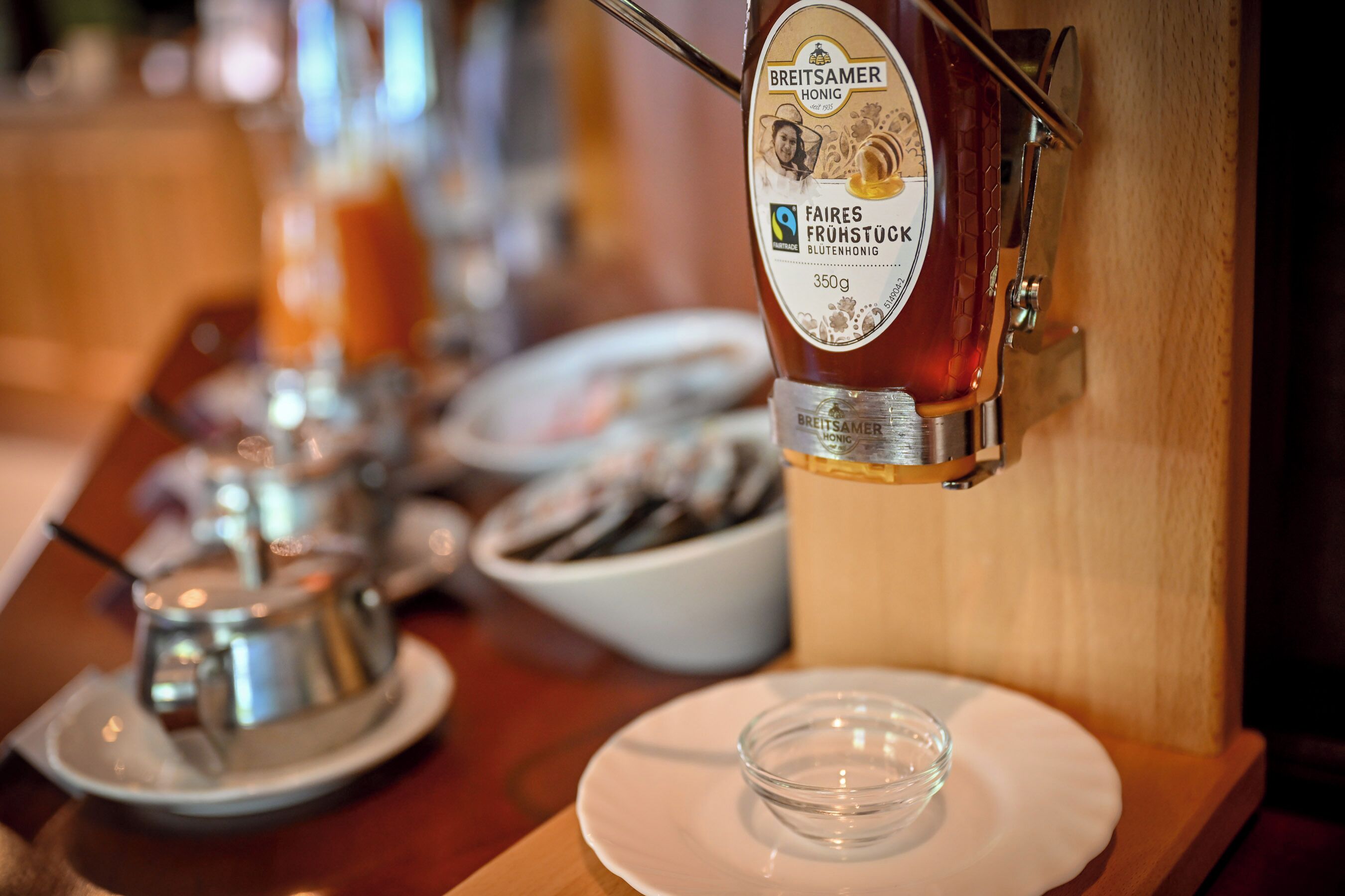 Uma área de bar com uma torneira de cerveja com a etiqueta 'Breitsamer Honig' e um copo de cerveja sobre um prato branco.