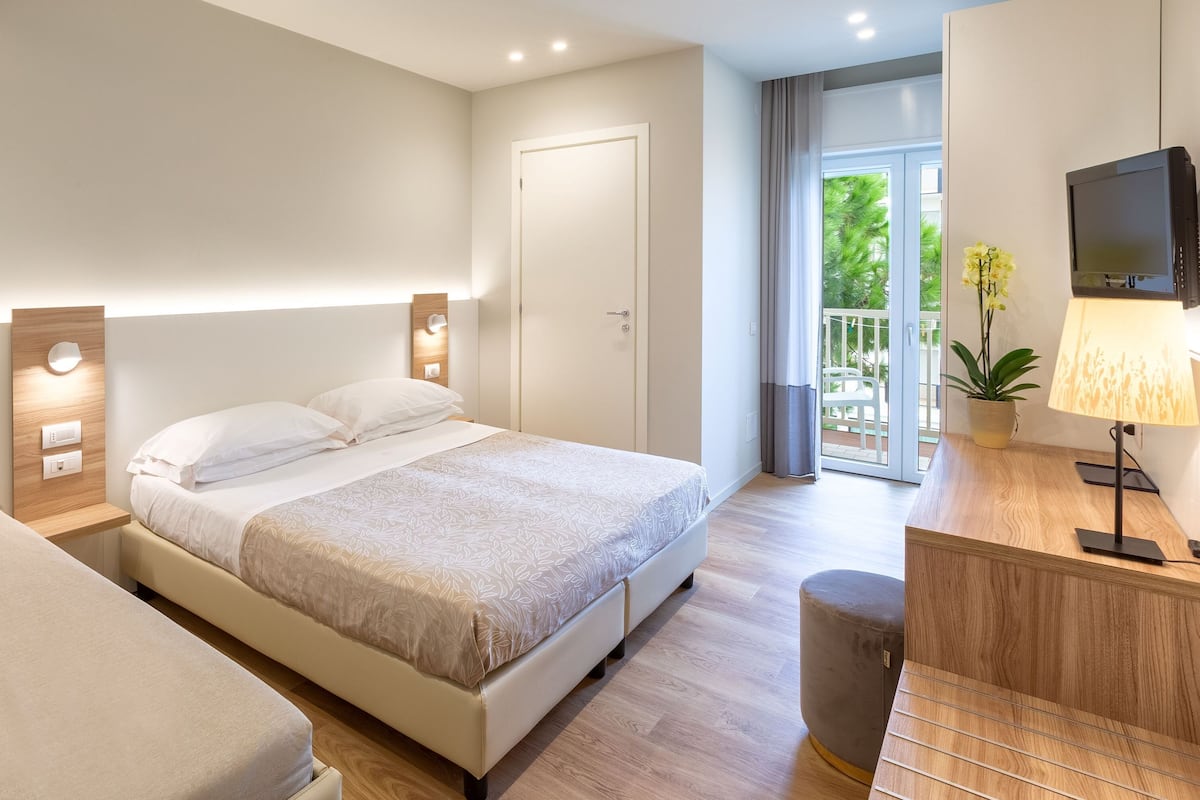 A modern hotel room with a bed, a sofa, a desk with a lamp, and a TV.
