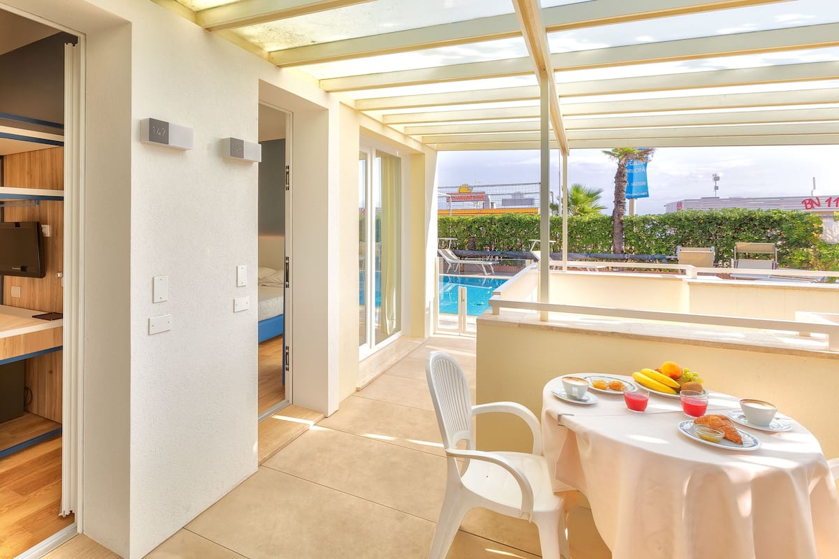 A room with a bunk bed, a small table with breakfast, and a view of a swimming pool.