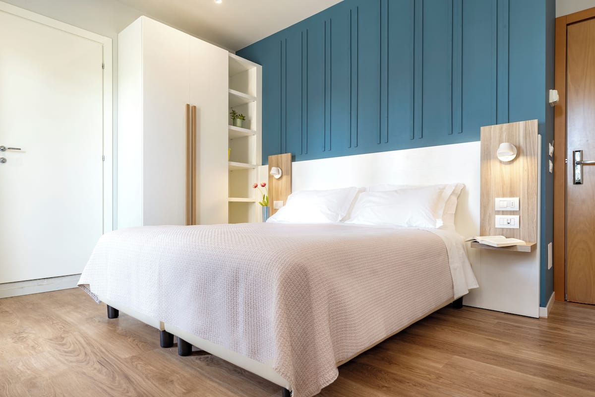 A neatly arranged bedroom with a bed, a built-in shelf, and a door.