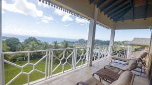 A balcony with a view of the ocean and greenery, furnished with lounge chairs and a table. - Forst Villa (Kingstown)