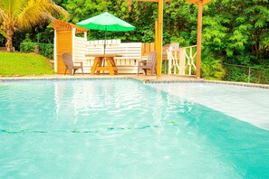 A swimming pool with a wooden deck, two chairs, and a green umbrella. - Forst Villa (Kingstown)