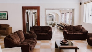 A spacious living area with multiple brown sofas, a coffee table, and a checkered floor. - Alzira Granada Hotel (Sao Lourenco)