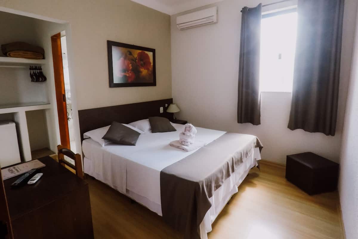 Ein Hotelzimmer mit Bett, Schreibtisch mit Stuhl, Schrank, einem Gemälde an der Wand und einer Klimaanlage.