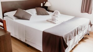 A neatly made bed with white and brown linens, a folded towel, and a bedside lamp. - Alzira Granada Hotel (Sao Lourenco)