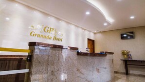 A hotel reception area with a marble counter, a reception desk, a television mounted on the wall, and a sign that reads "Granada Hotel". - Alzira Granada Hotel (Sao Lourenco)