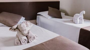 Duas camas de solteiro com cabeceiras marrons e roupa de cama branca, uma toalha enrolada e uma escultura de toalha branca na cama à direita.