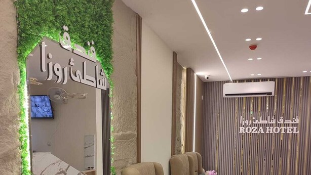 Uma área de recepção de hotel com balcão, televisão e área de estar com sofás e uma pequena mesa.