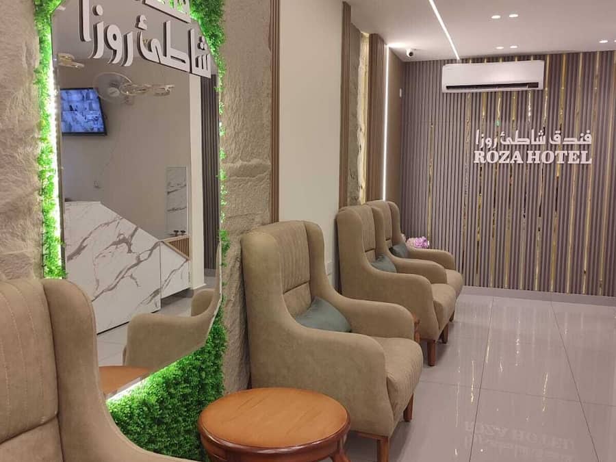 Zona de recepción de un hotel, con mostrador de recepción, televisor y área de estar con sofás y una mesa pequeña.